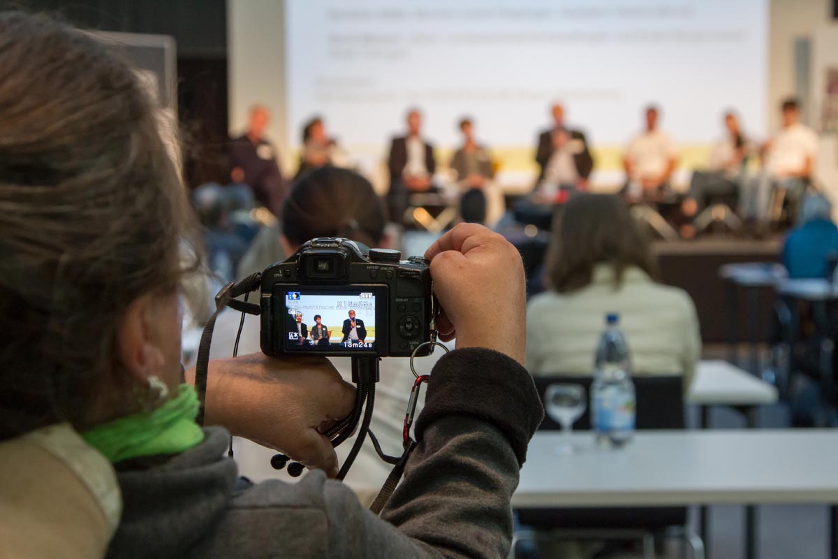 Talk-Runde: Blick auf das Podium im Display einer Kamera.