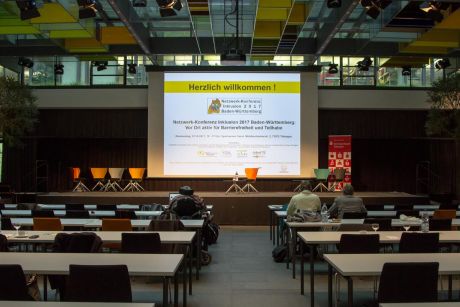 Der Veranstaltungsraum vor Beginn der Konferenz, Begrüßungsfolie ist auf der Bühne sichtbar.