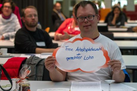 Abschlussrunde: Dominic Edler zeigt Plakat in Form einer Wolke mit Forderung aus Workshop 3: „Freie Arbeitsplatzwahl und gerechter Lohn“.